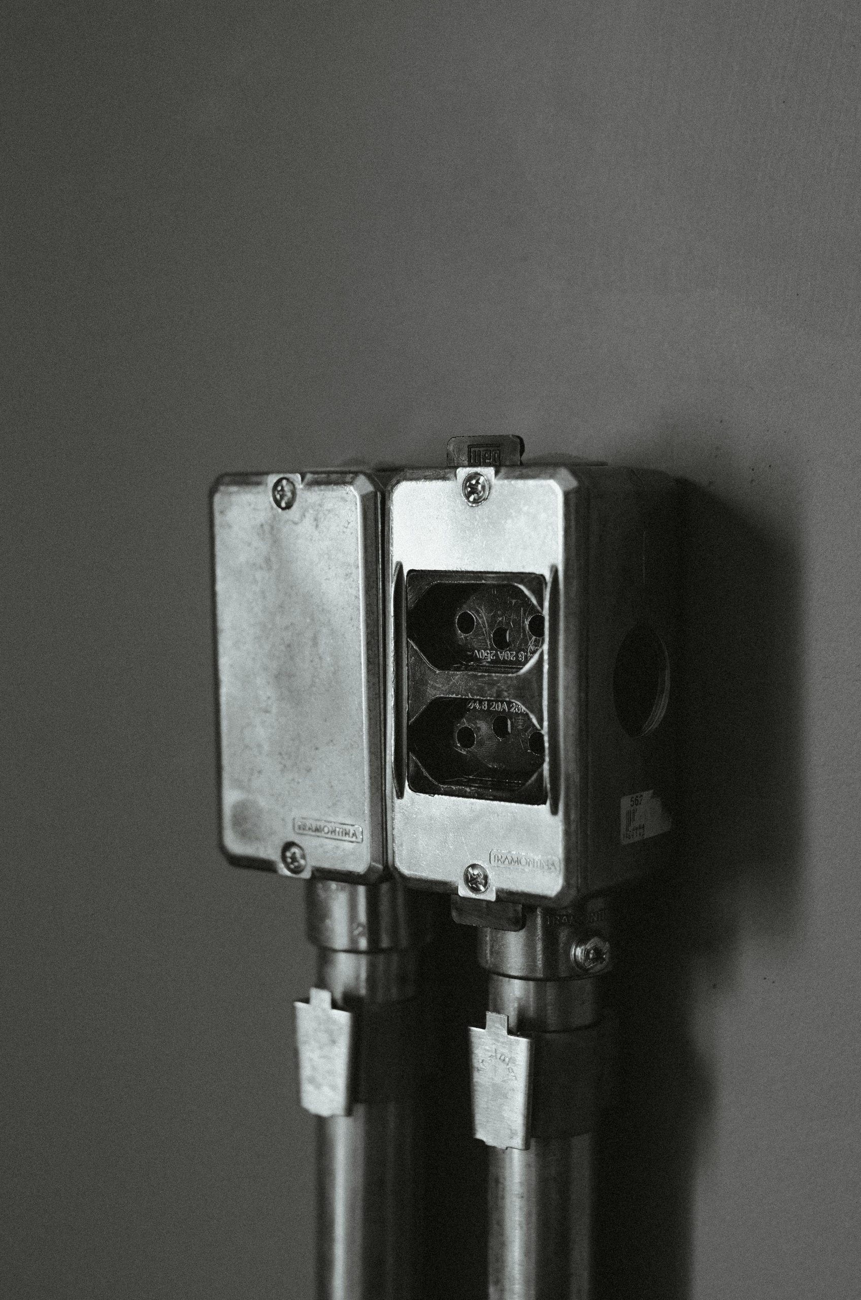 Monochrome image of a wall-mounted plug socket with metal pipes, showcasing industrial design.